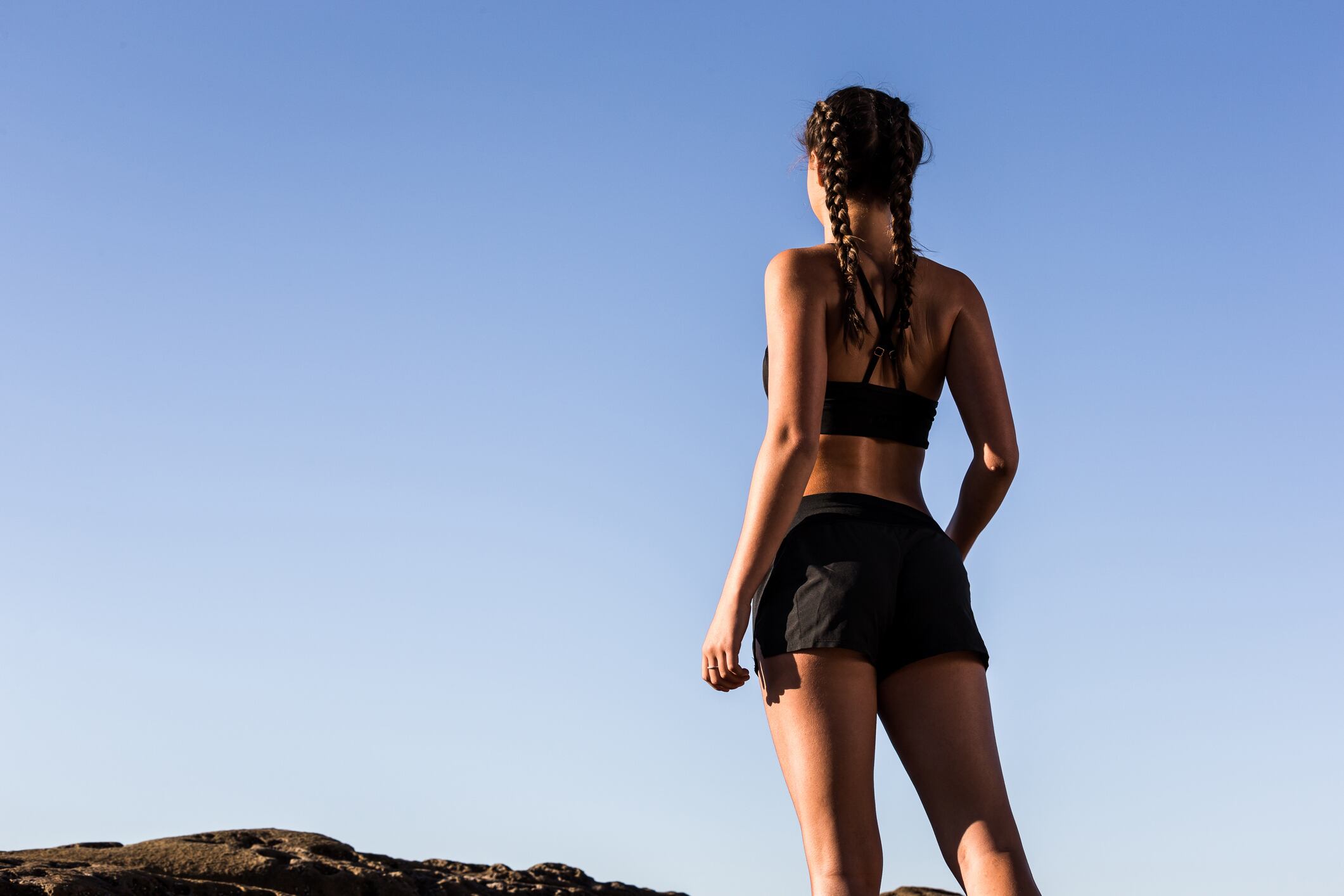 Woman runner, wearing black sports bra and shorts, looking out over the sunrise.
