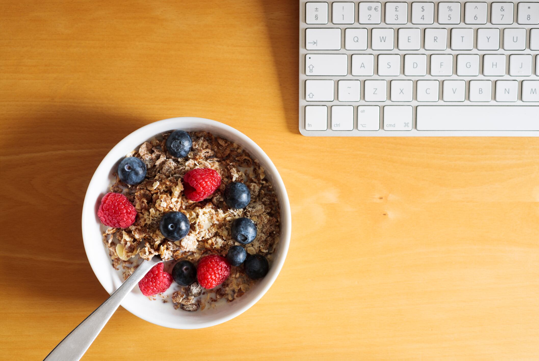 UK, breakfast cereal of muesli with fresh raspberries and blueberries on a desk with keyboard