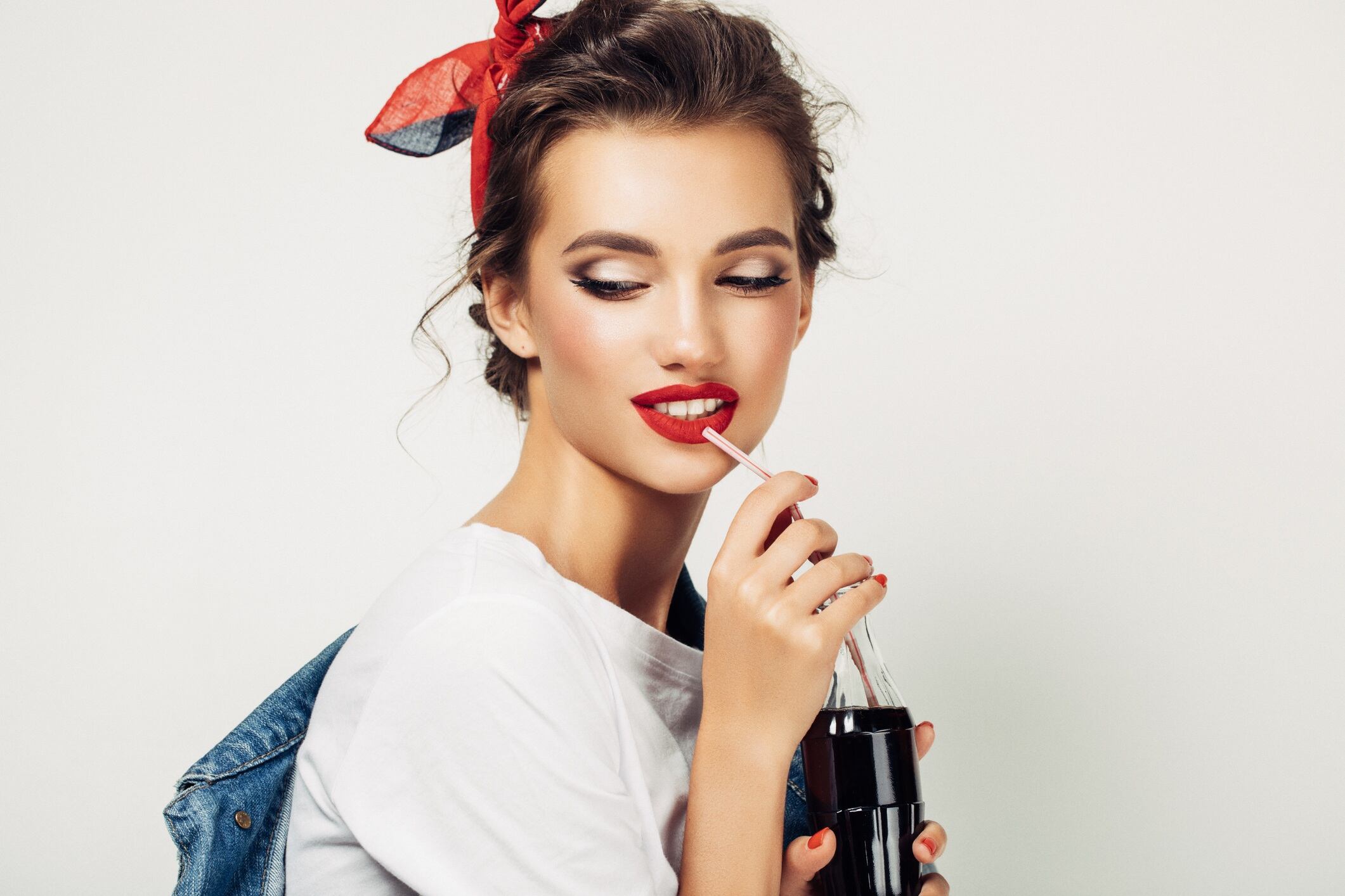 Woman wearing red headband and drinking from coke bottle.