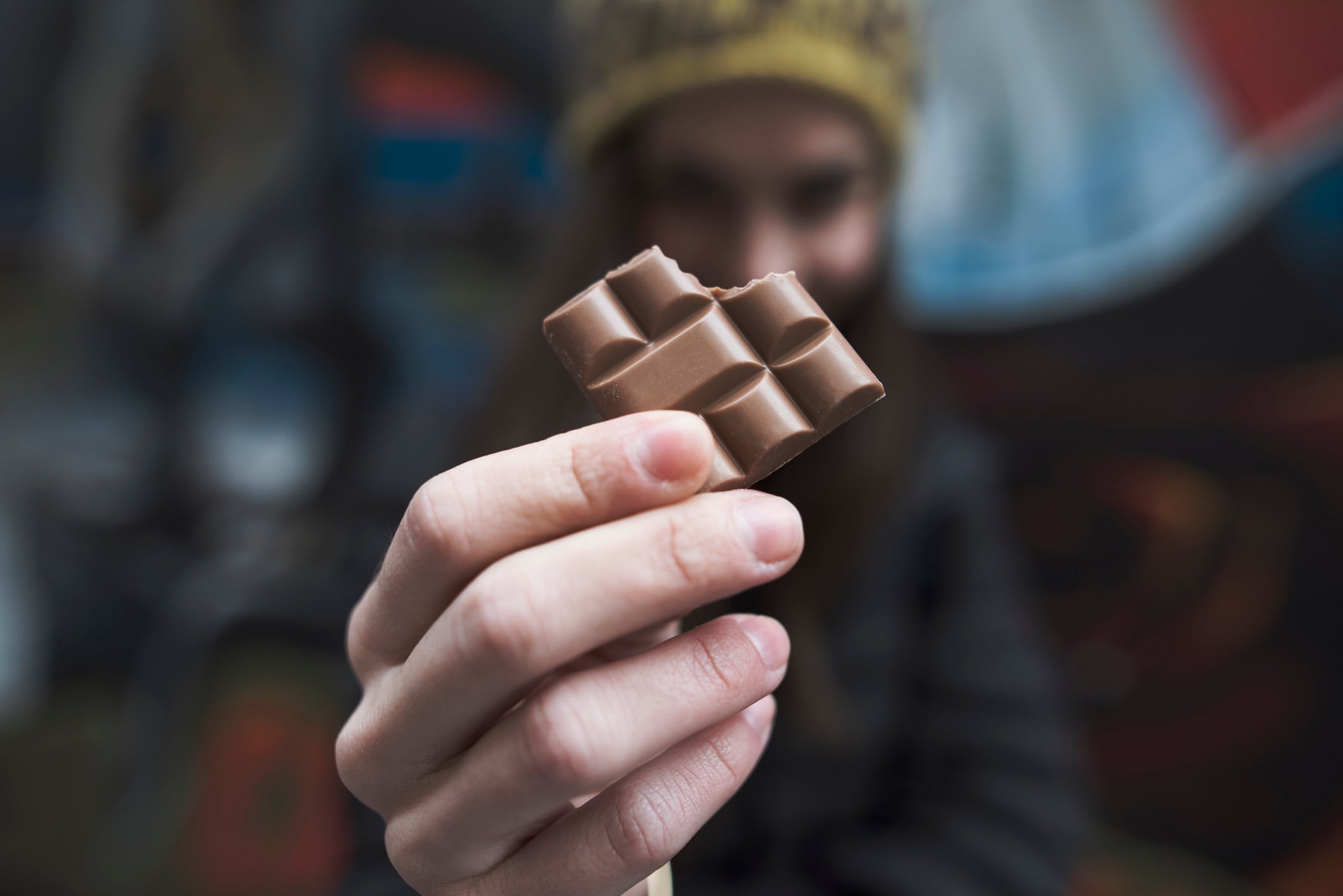 A woman holding up a bar of chocolate with a bite out of it.
