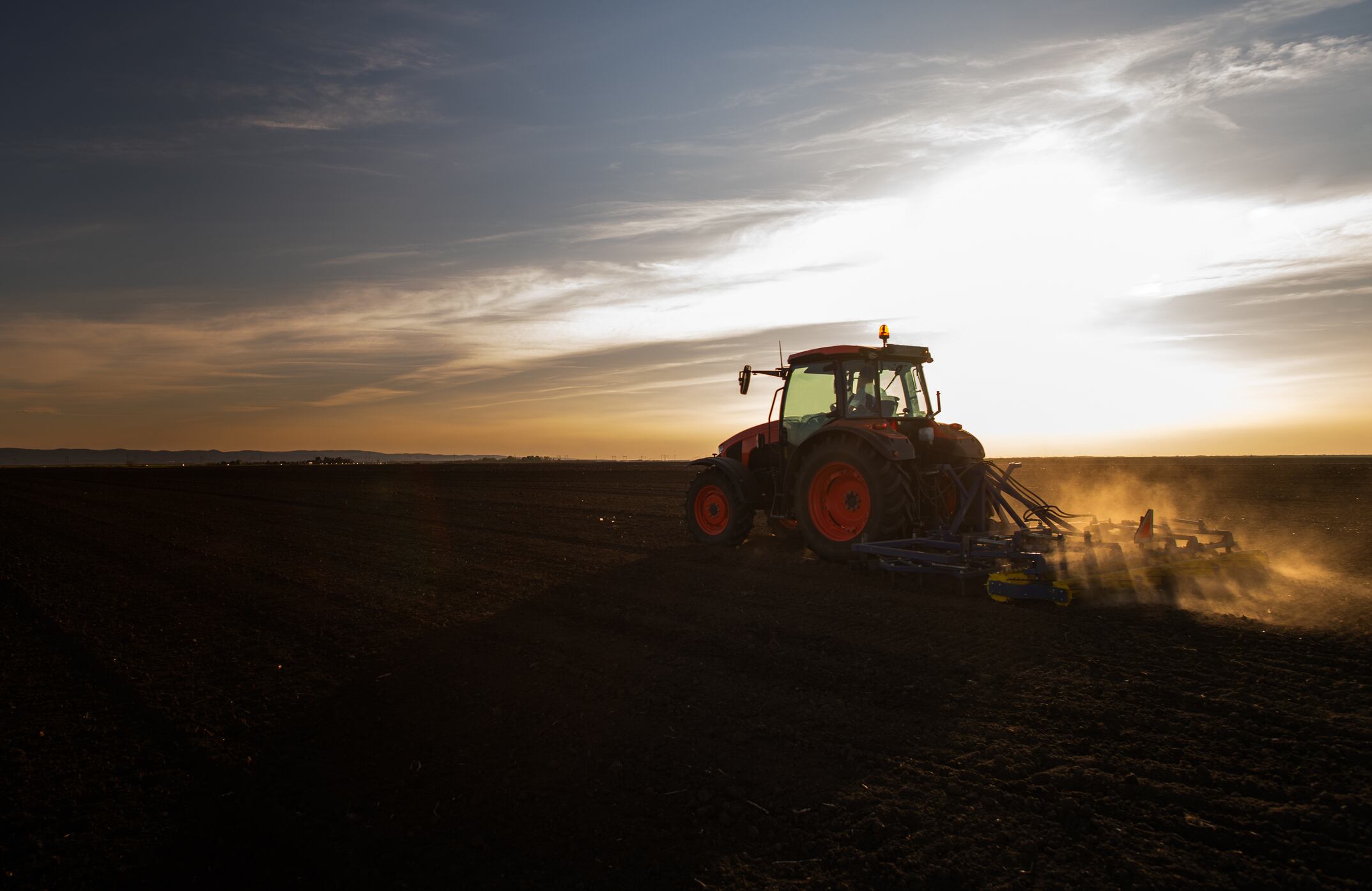Tractor plowing farm, preparing soil for new crop plantation during the evening.