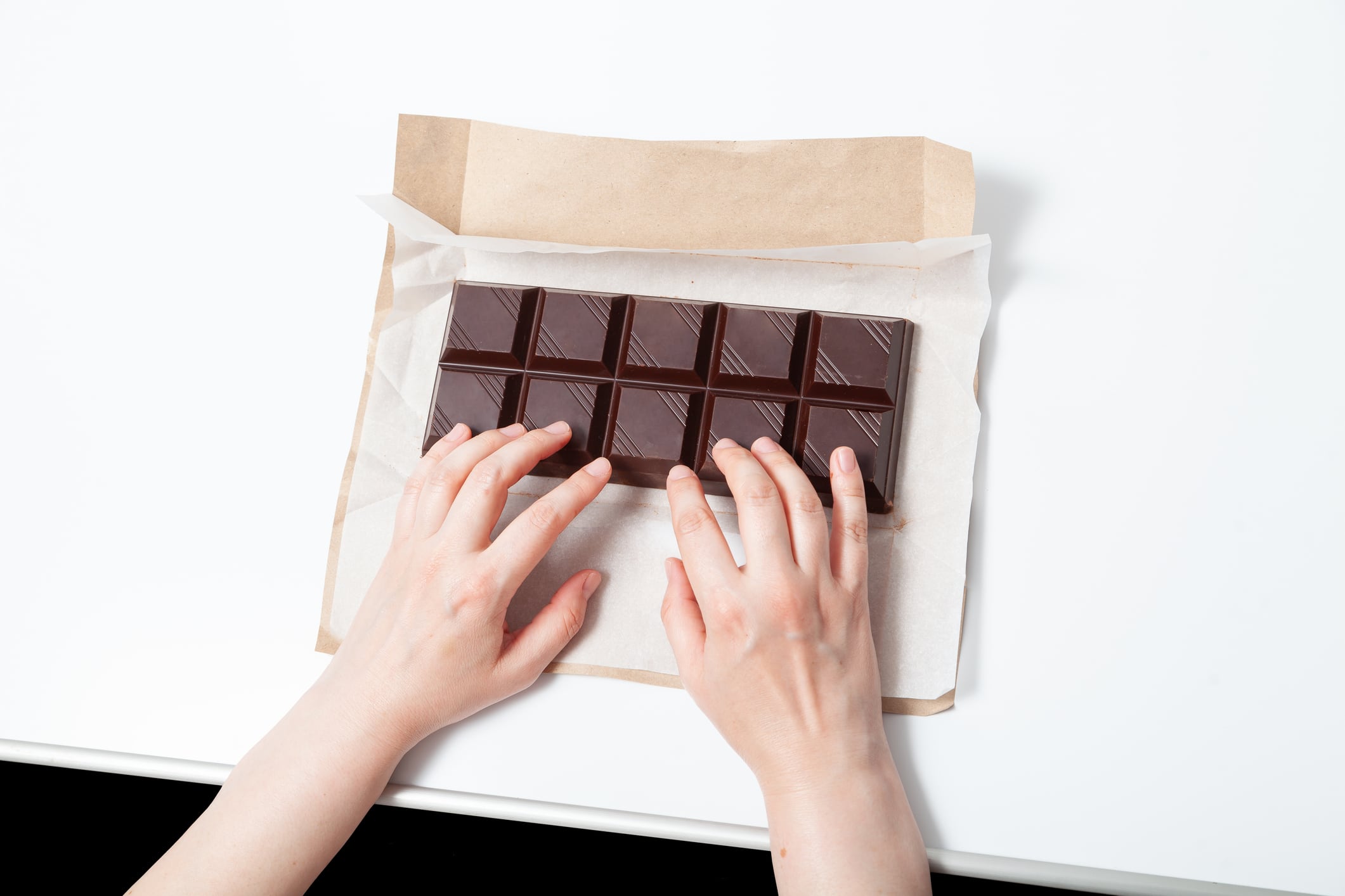 Hands rest on a large bar of dark chocolate. A comical comparison of a laptop keyboard with a bar of chocolate. Addiction to social networks and computer