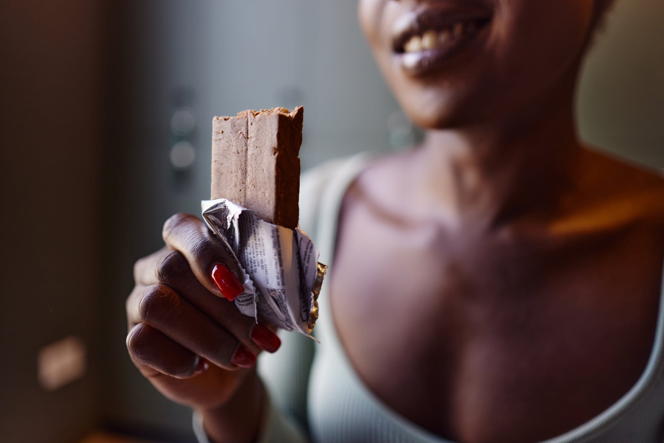 Mindful indulgence trend on the rise. Image: Close up of unrecognizable African American sportswoman eating protein bar after sports training in locker room.