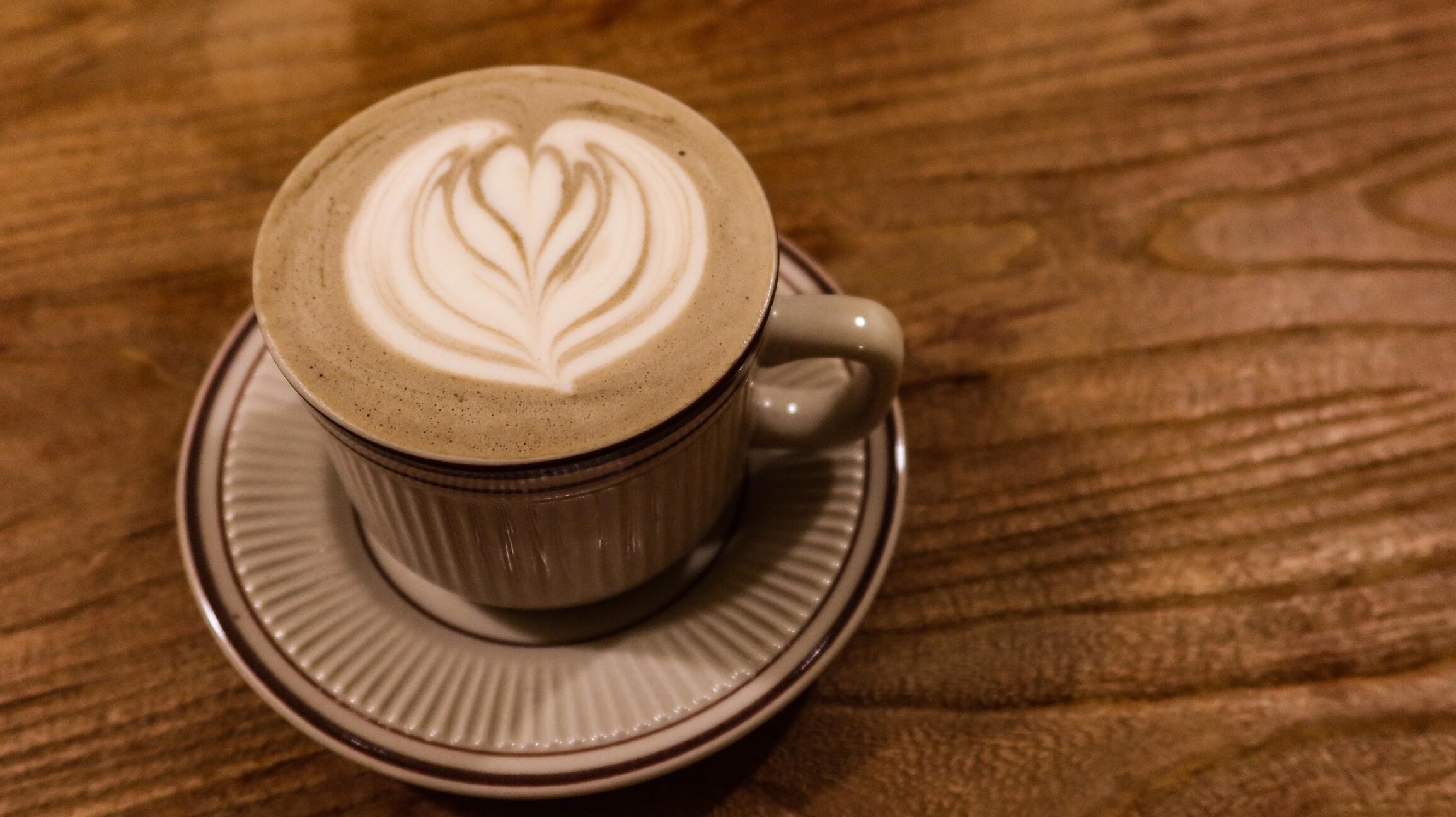 Hojicha latte with coffee art and foam on top in a mug.