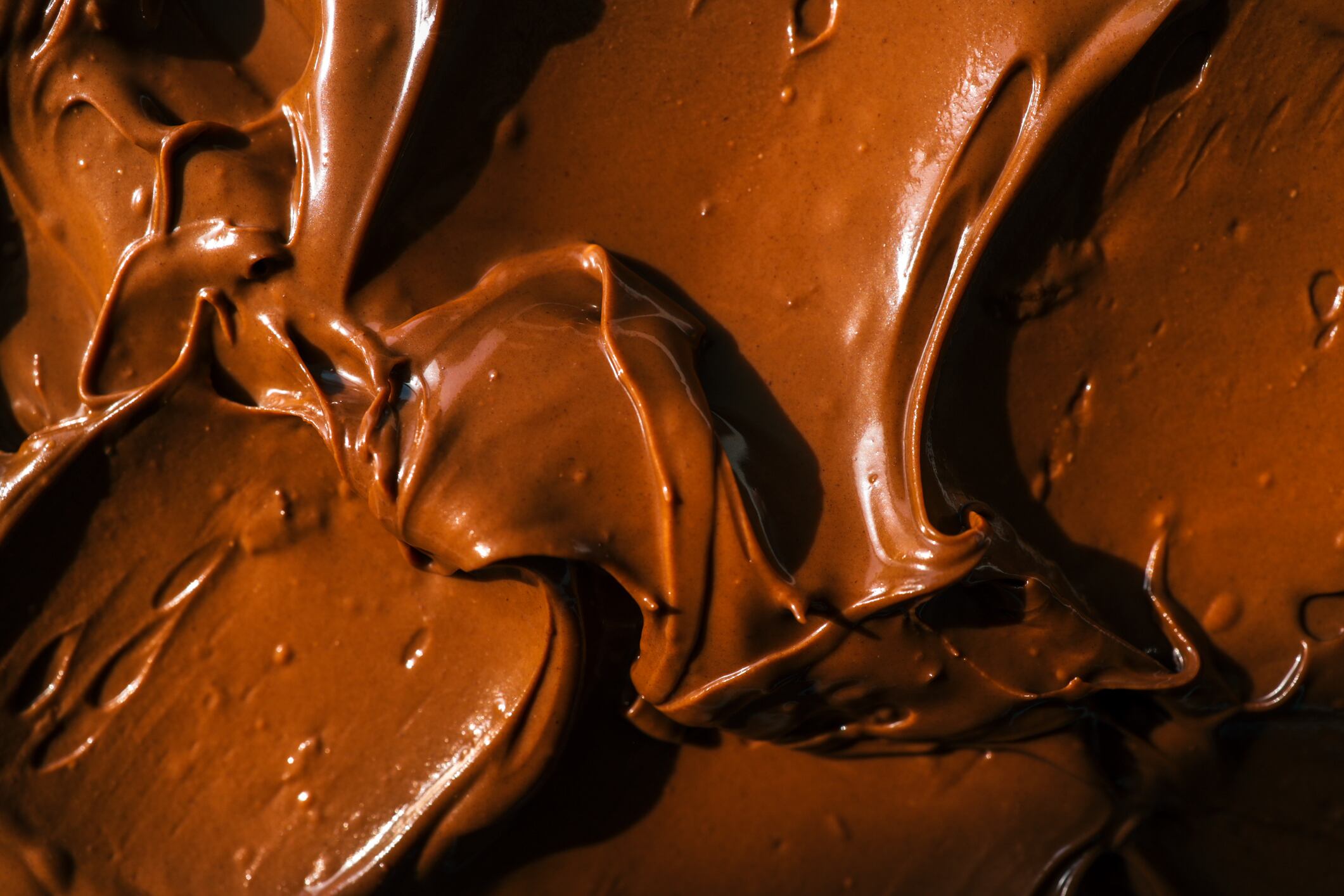 Close-up of smooth chocolate frosting with rich texture and deep brown color. The creamy, glossy surface has distinct swirls, highlighting its velvety consistency, perfect for cakes and desserts.