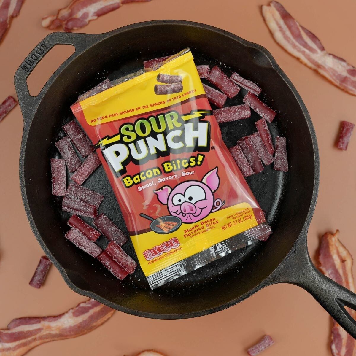 A pack of American Licorice Company Sour Punch Bacon Bites in a cast iron skillet with the sweets scattered all around.