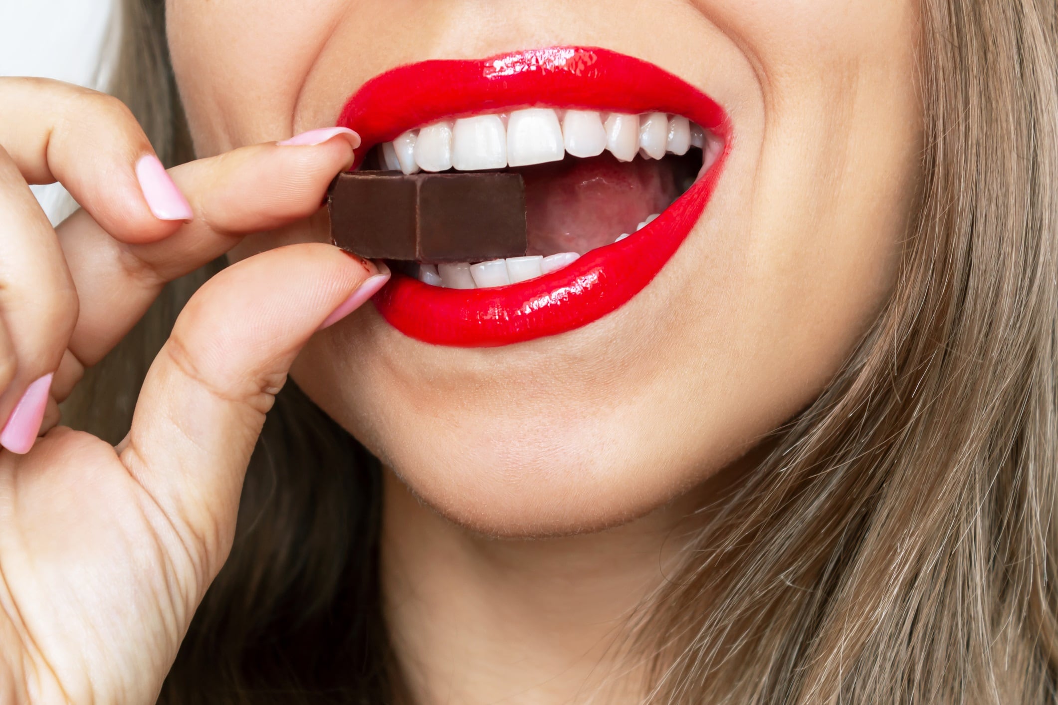 Cropped shot of a woman with red lips, eating dark chocolate.