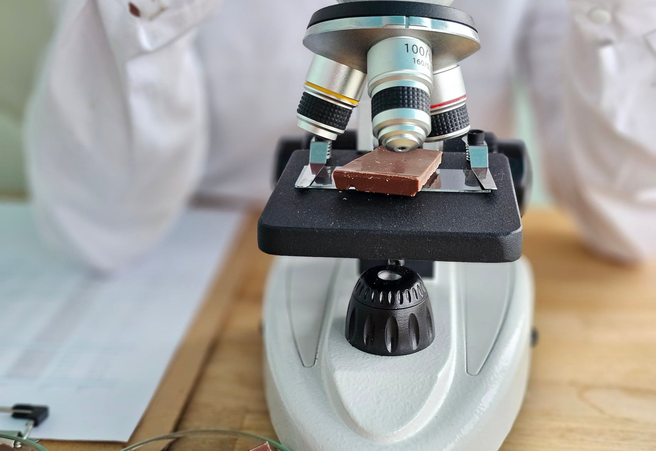 Scientist observes chocolate sample under microscope in laboratory for quality analysis and research insights
