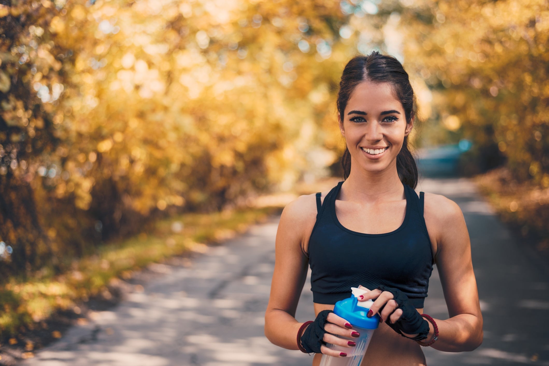 Woman in sportswear holding water bottle. Looking at camera.