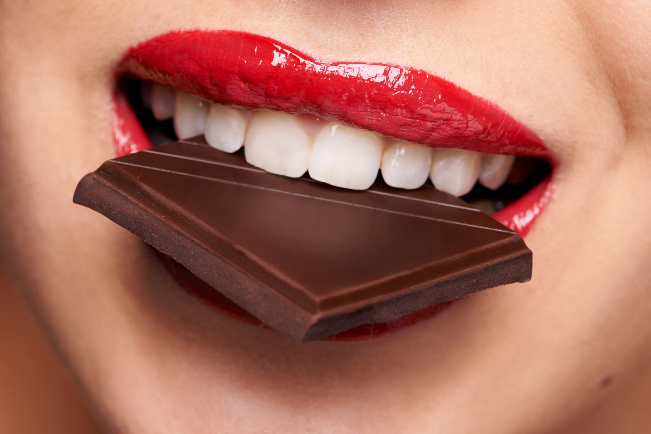 Woman with red lipstick biting into a piece of chocolate.