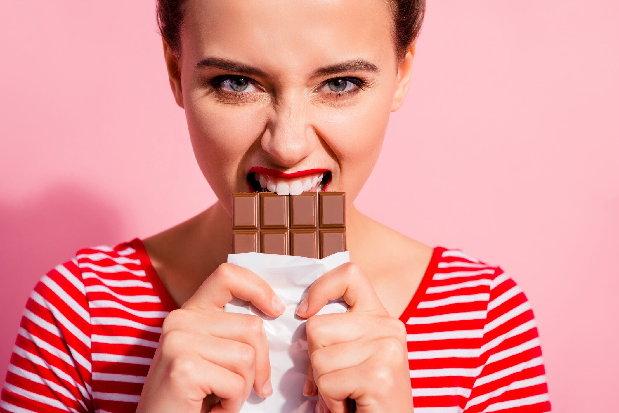 Woman wearing red and white-striped top, biting into a bar of chocolate.