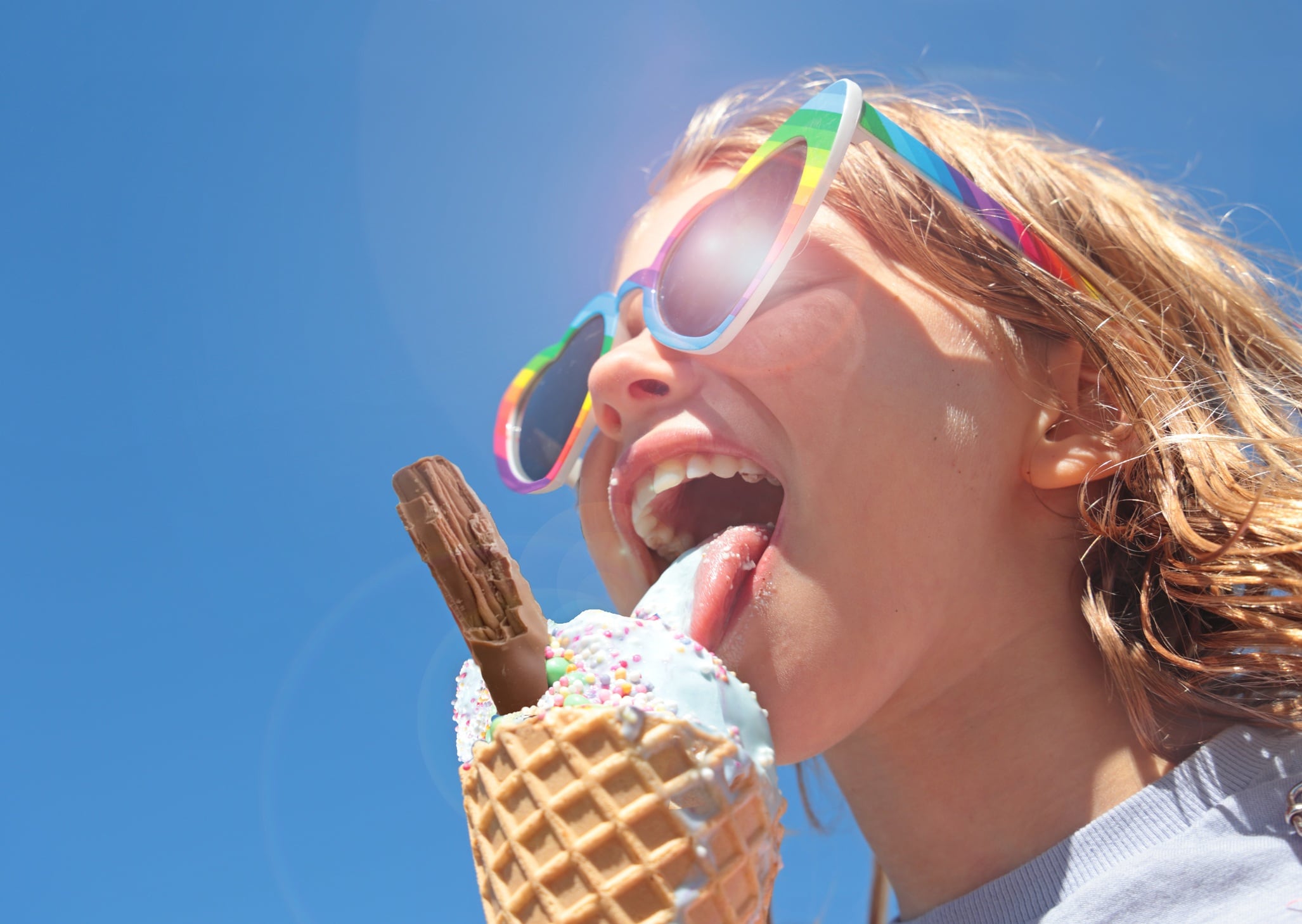 Young girl in sunglasses eating ice cream with a chocolate flake against blue sky