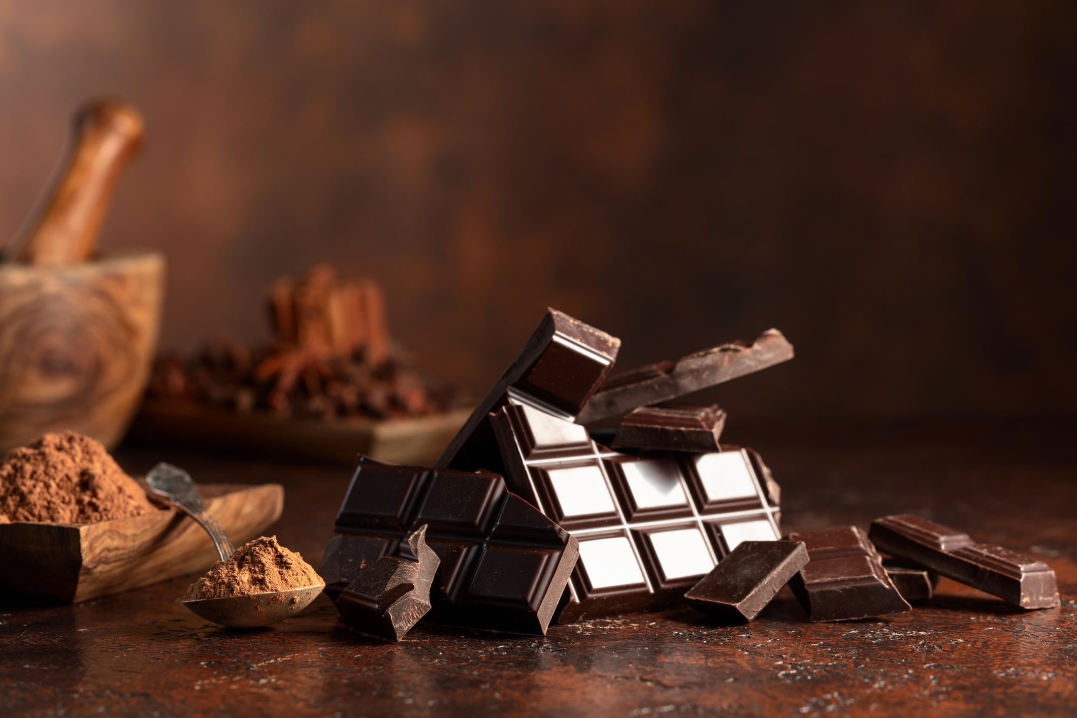 Bar of dark chocolate bar, with cocoa powder on a brown table.