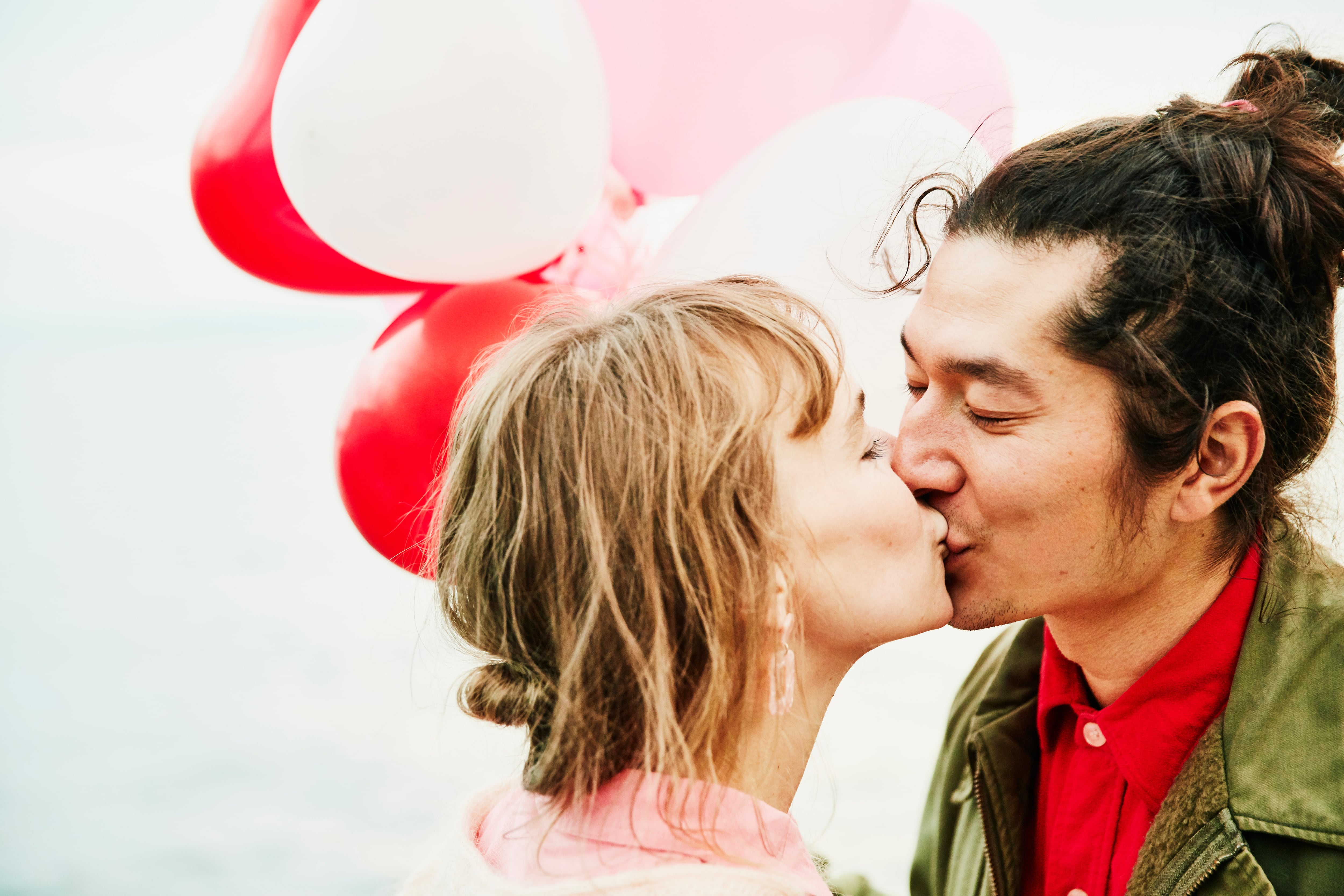 Couple holding heart shaped balloons kissing while on date