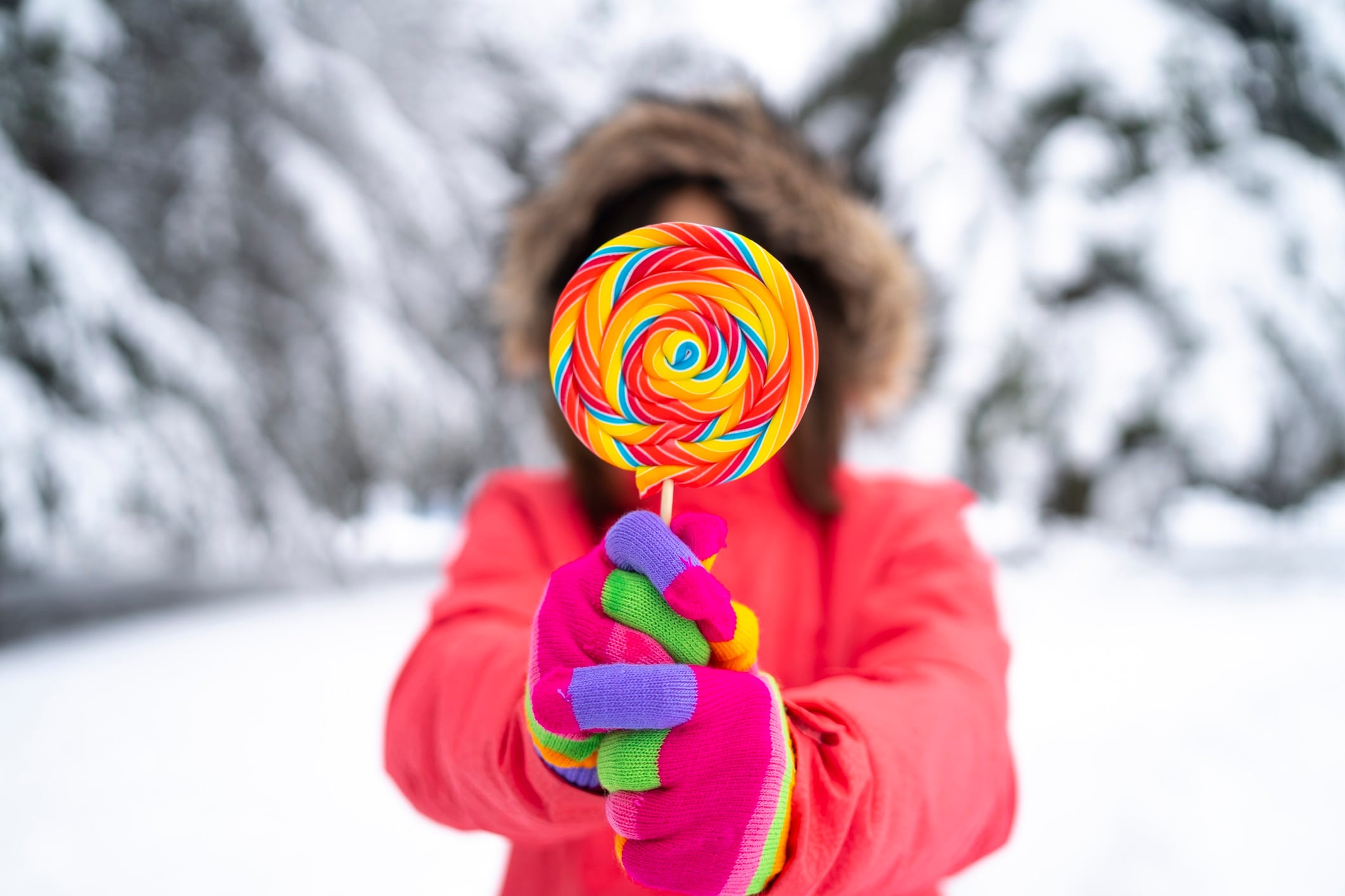 Young woman wearing colourful woolen winter gloves and pink jacket holding lollipop.