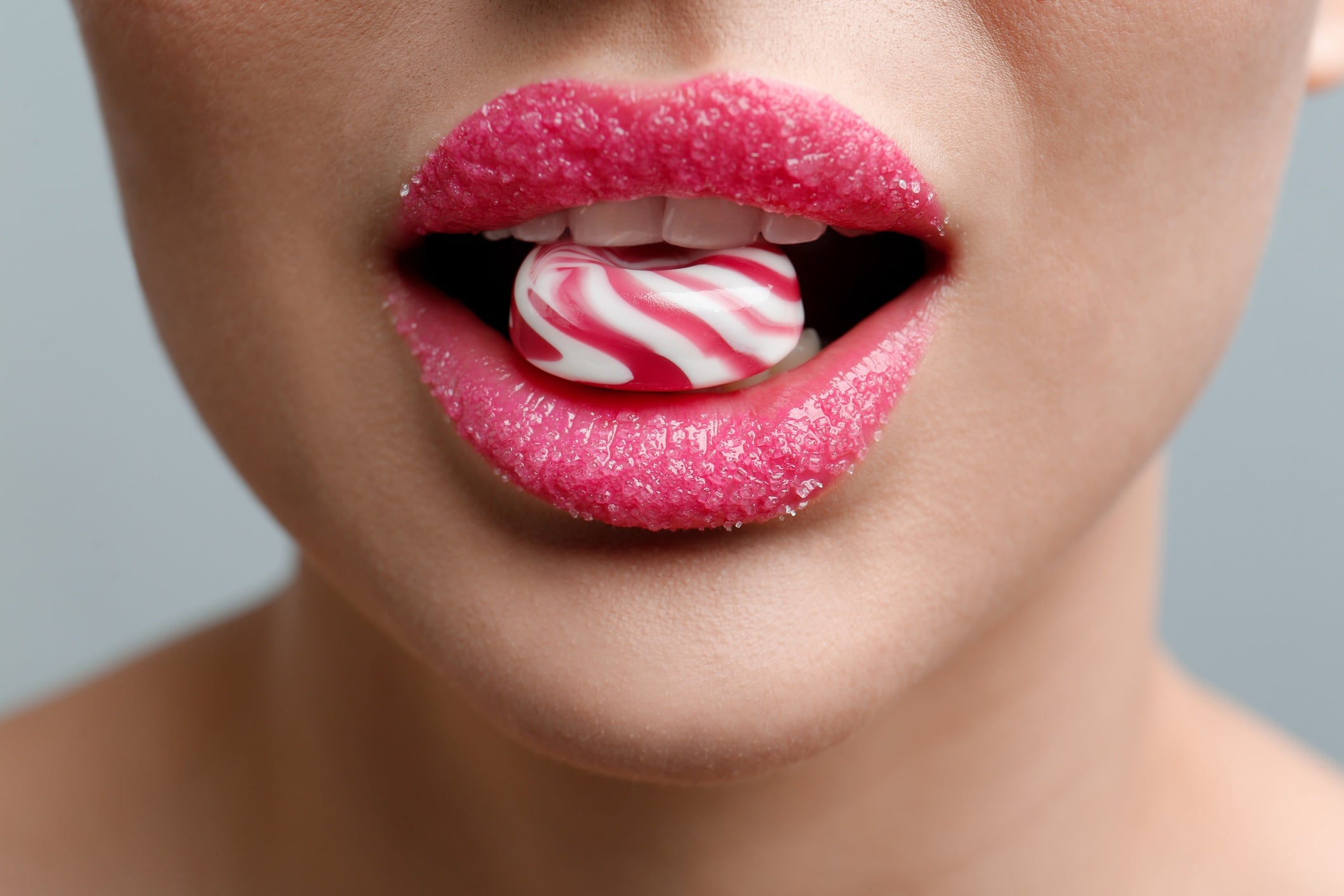 Close-up of woman eating sweet/candy, with lips covered in sugar. Grey background.