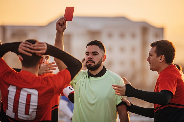 Group of people, male soccer match on a soccer field on winter day outdoors. Referee holds up red card.