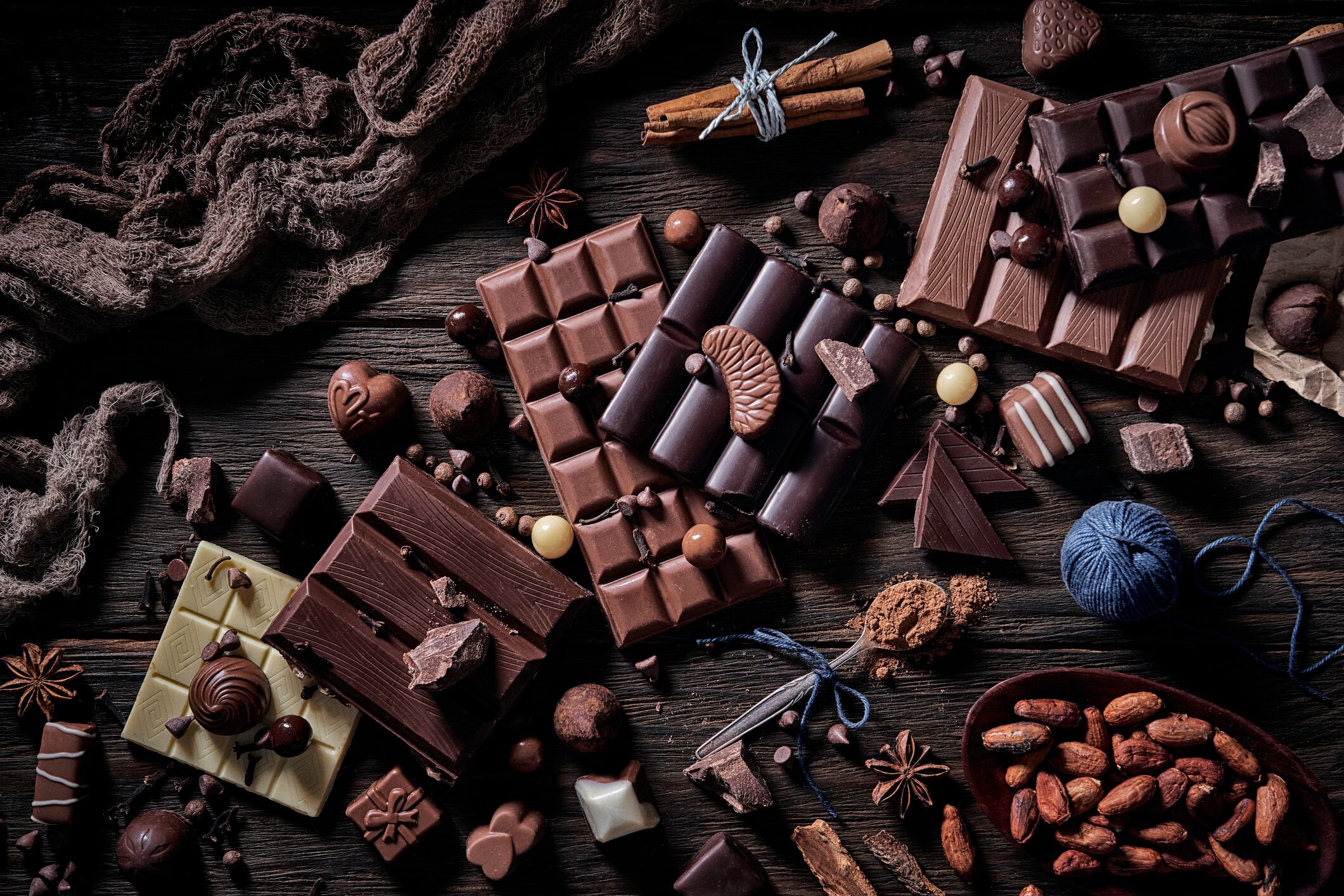 Assorted chocolate bars and cocoa beans on a wooden table.